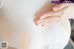 A woman in a white bodysuit is holding her breasts.