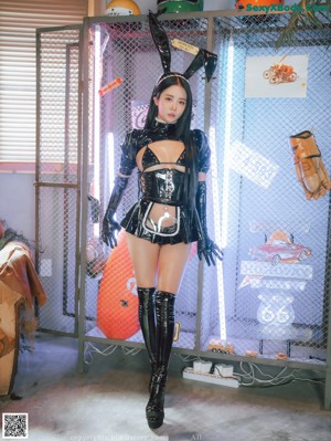 A woman in a black latex outfit sitting on the ground.