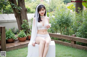 A woman in a white bikini sitting on a blanket in the grass.